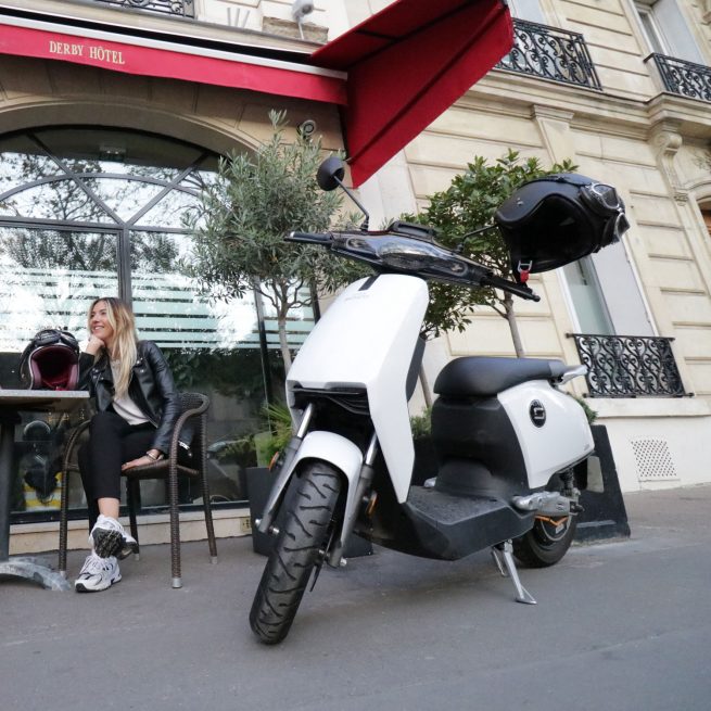 Jeune femme assise à la terrasse d'un café au côté de son Super Soco CU-X