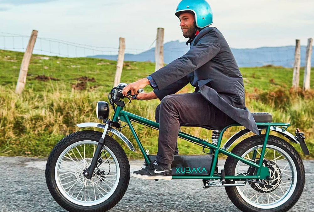 Une moto électrique Xubaka verte et son pilote, sur une route de campagne