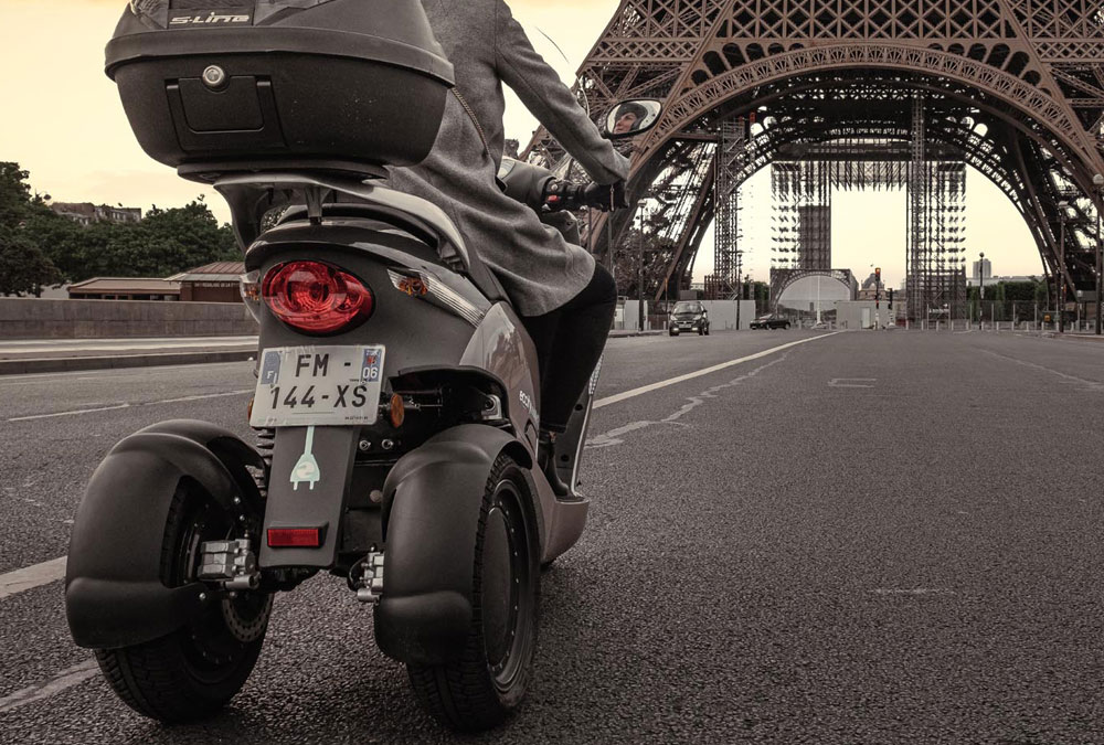 un scooter 3 roues passant près de la Tour Eiffel