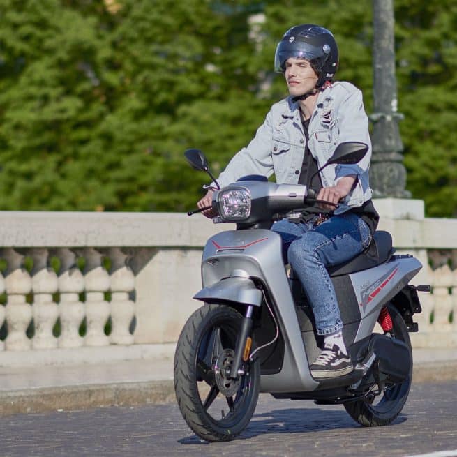 Sur un pont, jeune homme au guidon d'un askoll NGS2