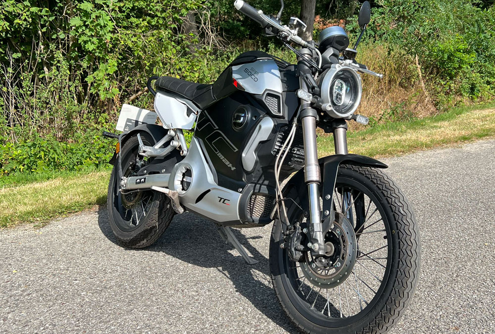 La moto électrique Super Soco TC MAX, garée près d'une forêt