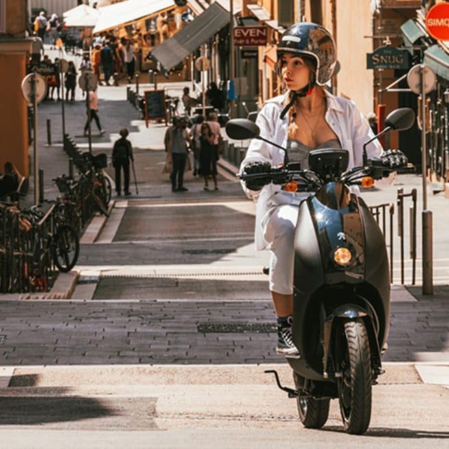 Jeune femme sur un Peugeot E-Ludix dans les rues d'une petite ville